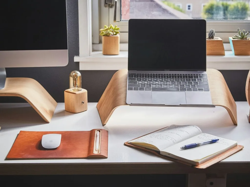 Ergonomische thuiswerkplek met een laptop op een laptopstandaard met daarvoor een muis op een muismat en een notitieboekje