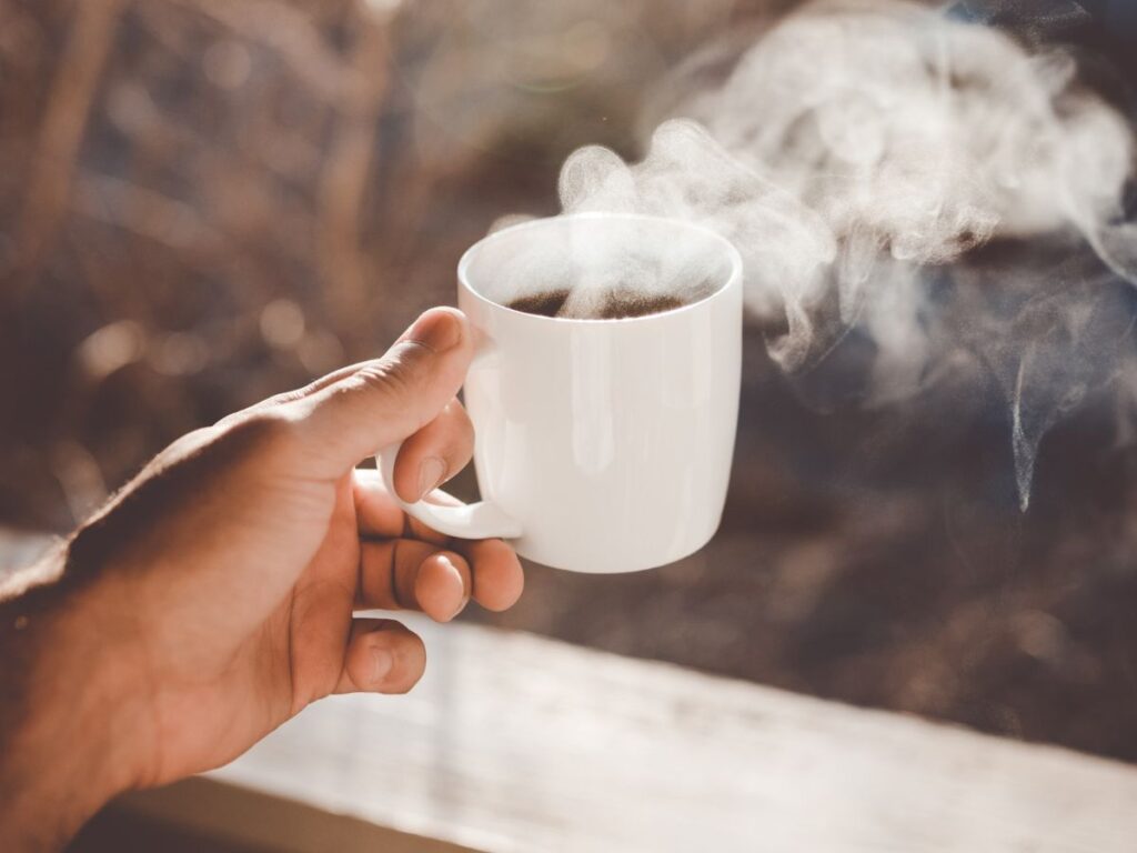 Geniet van goede koffie tijdens het thuiswerken - Hand met kop koffie in de tuin