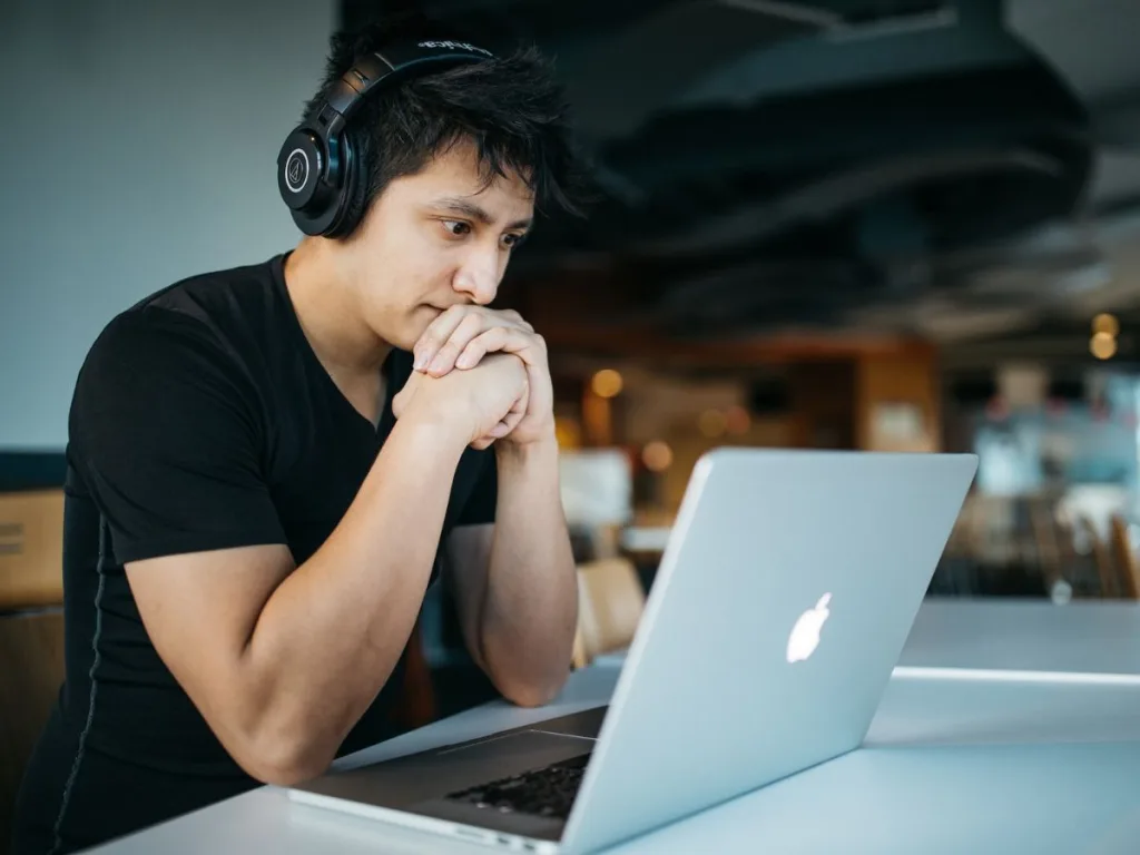 Man zit geconcentreerd te werken achter een laptop met een koptelefoon op