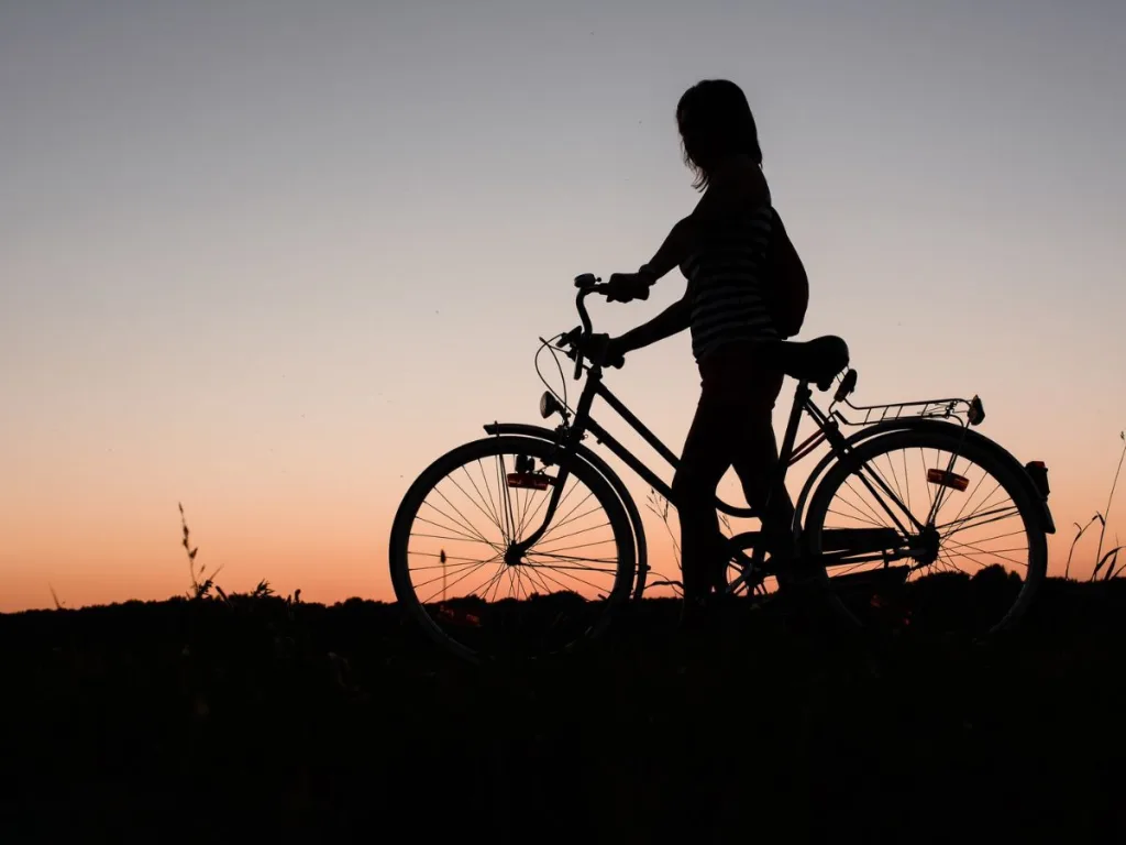 Vrouw staat met een fiets aan de rand van de natuur na een dag fietsen
