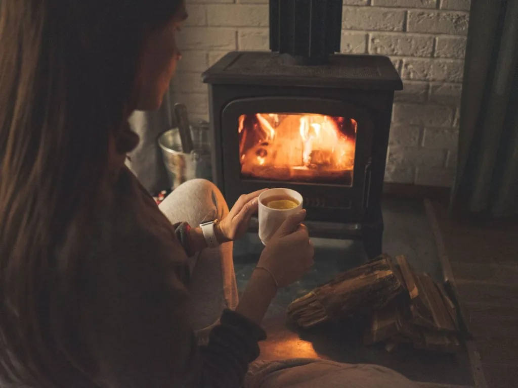 Vrouw zit in een knus huis met een warme drank voor een haard
