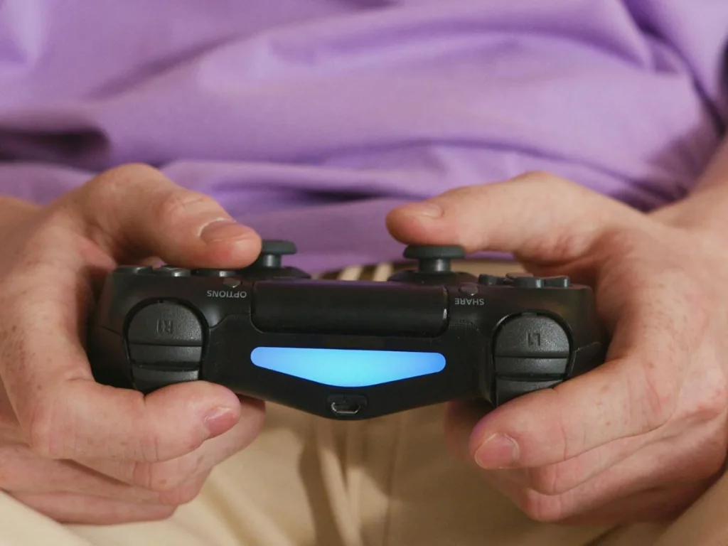 Man zit met een zwarte PlayStation 4 controller in zijn handen op de bank te gamen nadat hij de keuze heeft gemaakt tussen een Ps4 of een Ps5 spelcomputer