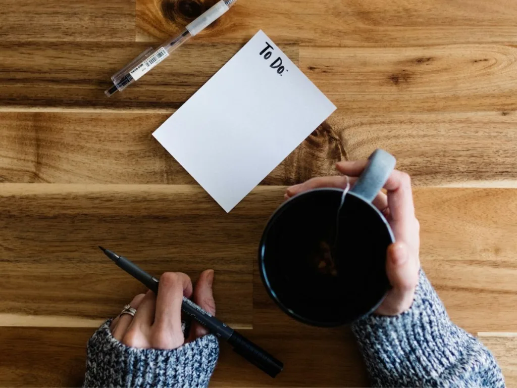 Vrouw zit met een notitieblok met to-do-lijst en een kop thee aan tafel om het klussen in huis efficiënt voor te bereiden